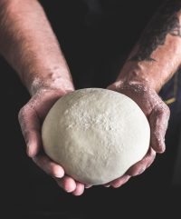 Chef holding a ball of fresh made dough in palm of hands.