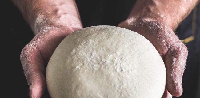 Chef holding a ball of fresh made dough in palm of hands.